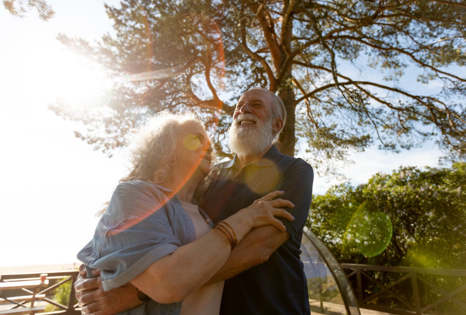 Casal de idosos sorridentes abraçados ao ar livre sob a luz do sol