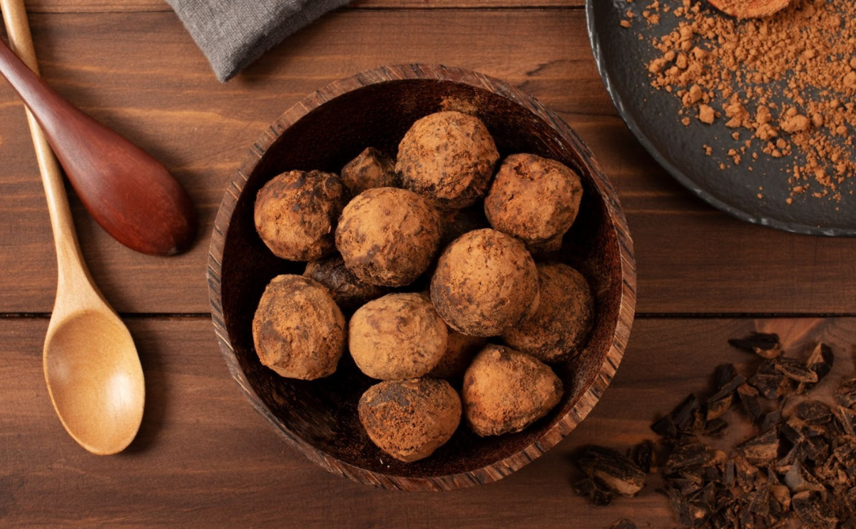 Taça com bolinhas energéticas de tâmaras, cacau e amendoim em cima de uma mesa de madeira