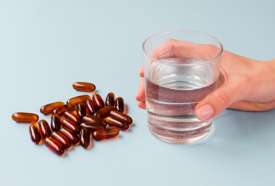 mão a segurar copo de água ao lado de comprimidos de cobre