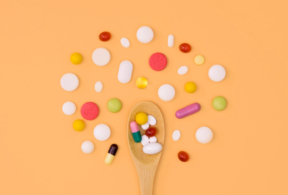 Colher de pau com multivitaminicos com diversas cores e formatos sobre fundo laranja