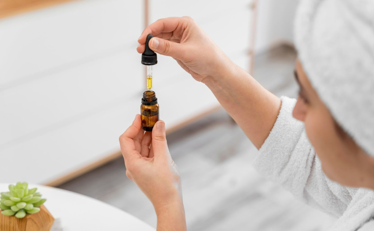 Mulher a tirar óleo essencial de um pequeno frasco de vidro utilizando a pipeta