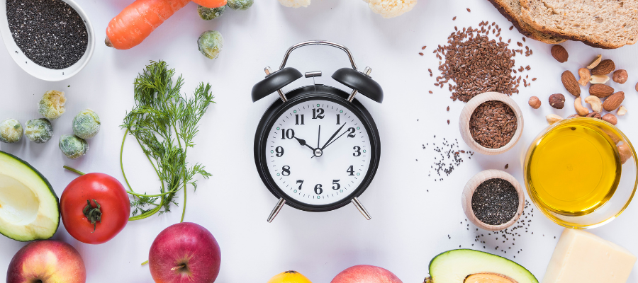 Relógio e alimentos saudáveis dispostos num fundo branco