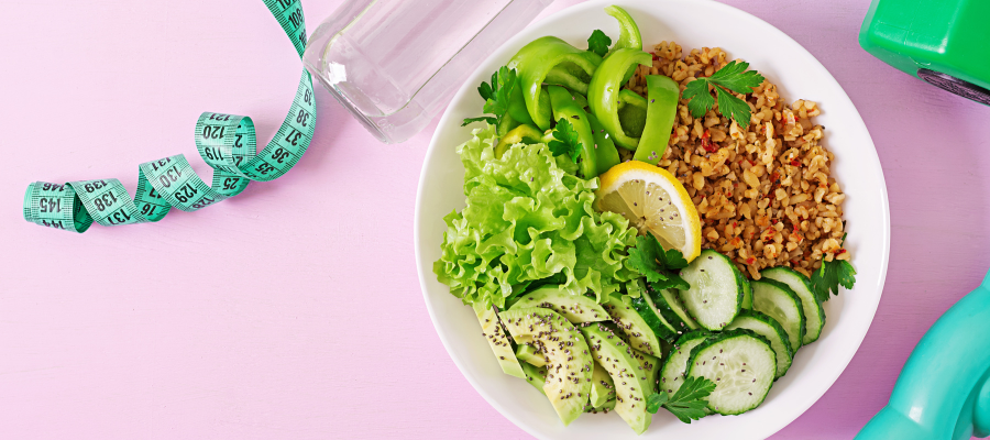 Prato de salada com halteres e fita métrica ao lado sobre fundo rosa