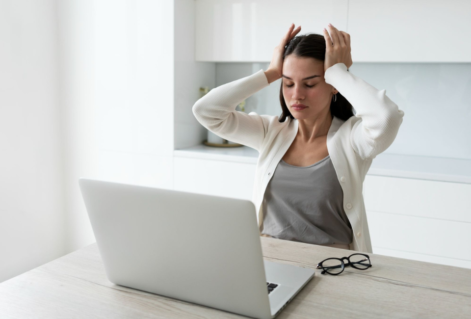 Mulher sentada às mesa a trabalhar num portátil, com as mãos na cabeça, com a sensação de stress.