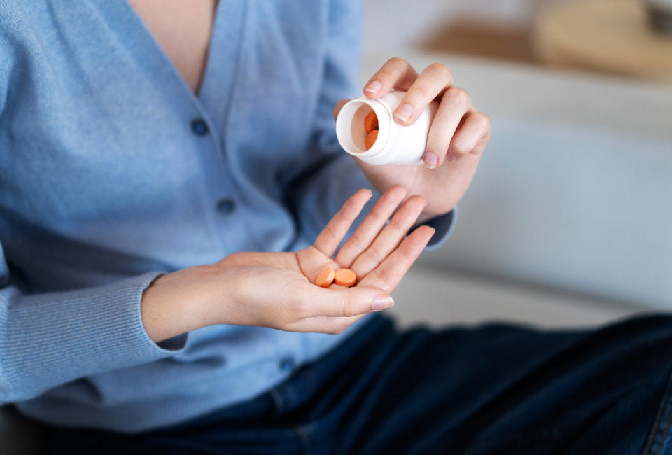 mulher com camisola azul a verter comprimidos cor de laranja de um frasco para a mão  
