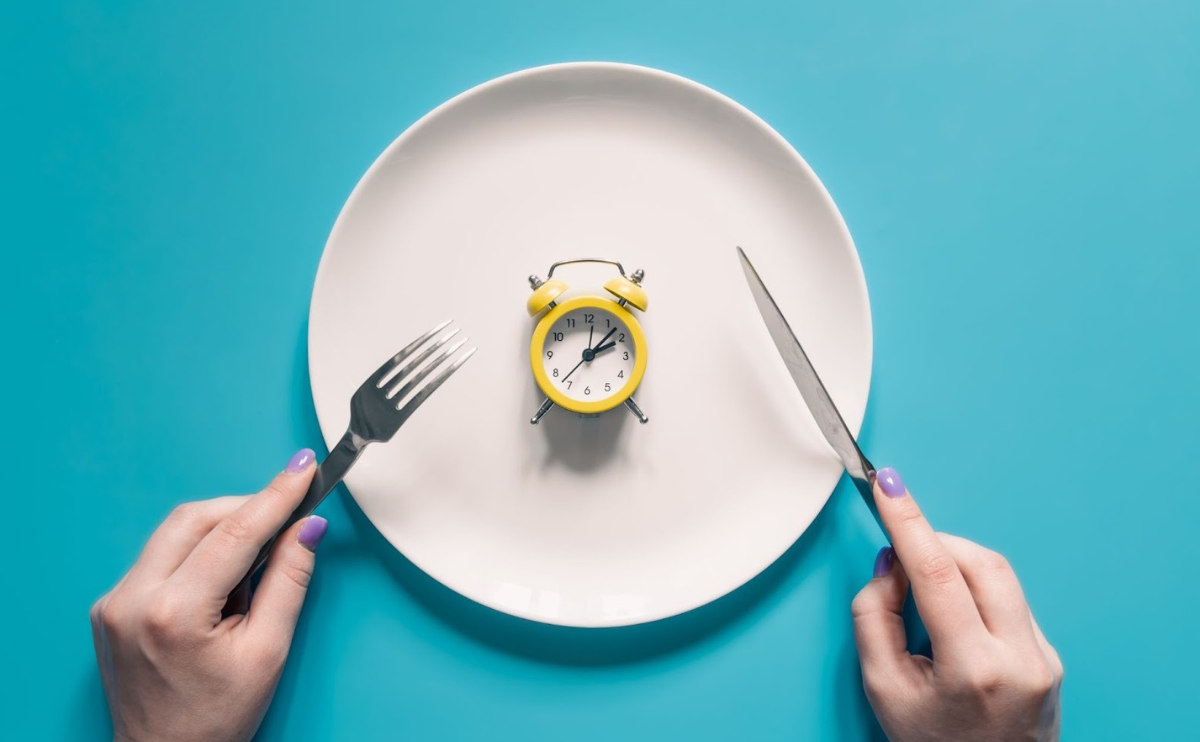 pessoa de faca e garfo na mão a comer de prato com pequeno relógio despertador 