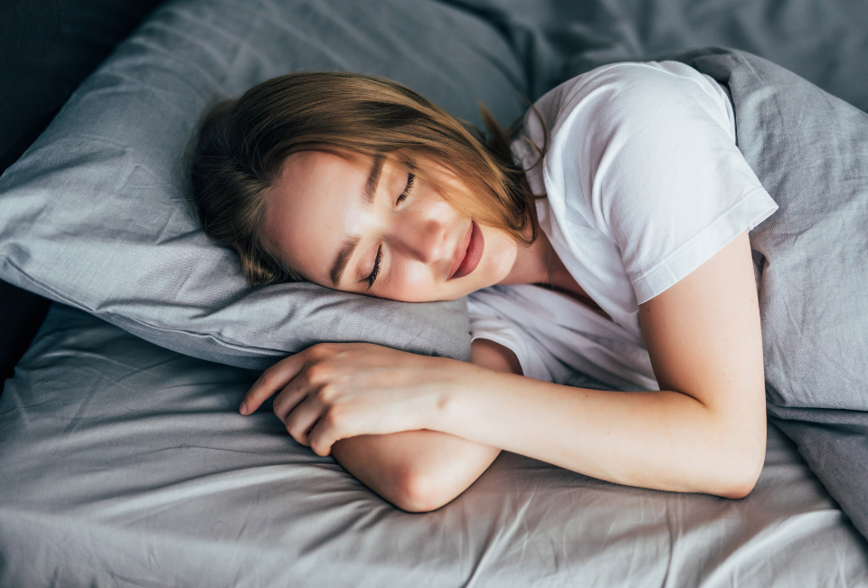 Uma mulher a dormir em paz, deitada de lado numa almofada e coberta por lençóis cinzentos