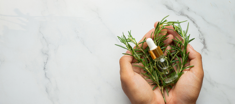 mãos a segurar oleo essencial de alecrim com um fundo marmore