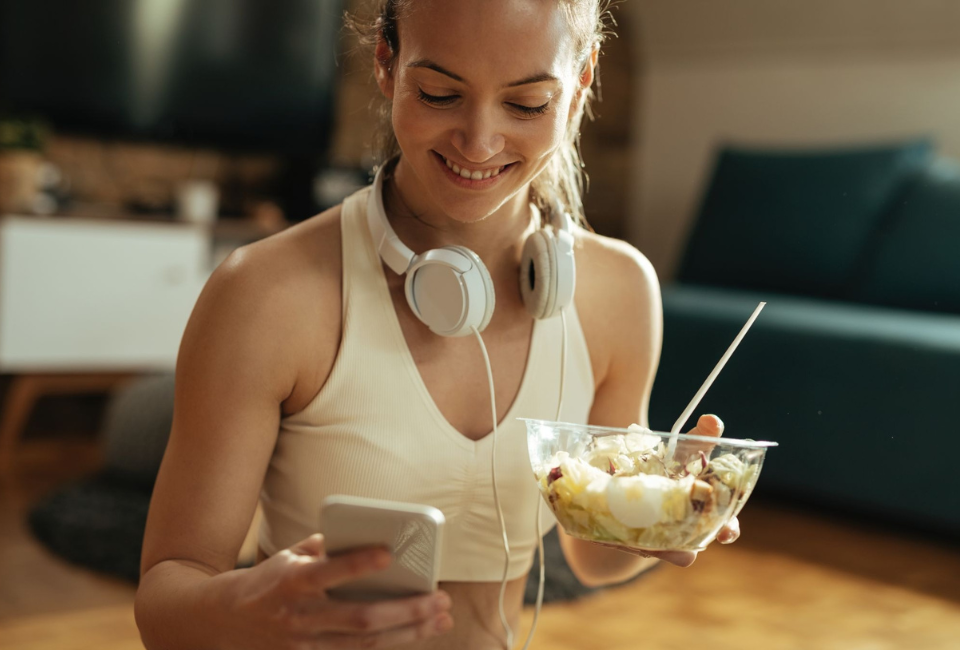 Mulher sentada à mesa a comer uma bowl de iogurte, cereais e fruta.