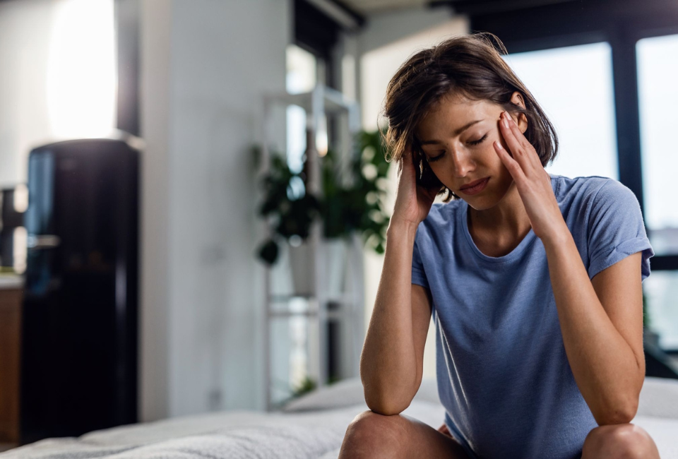 Mulher triste, com dor de cabeça, sentada na cama com os olhos fechados 