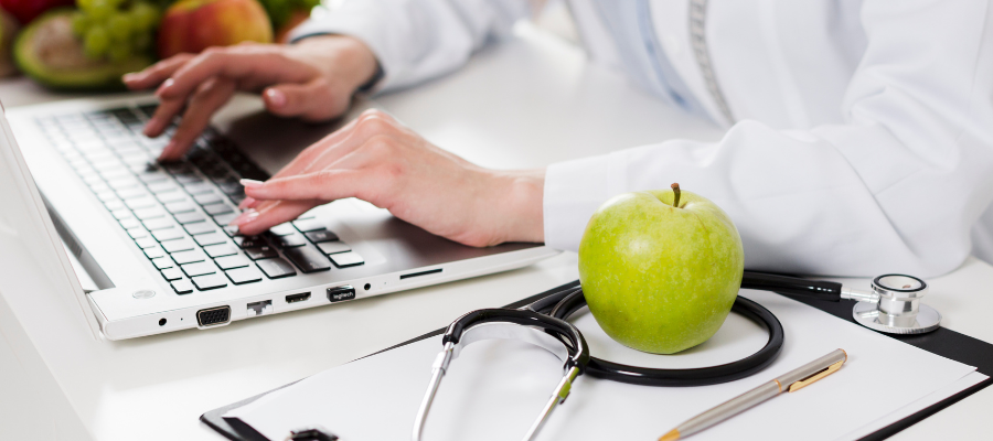 nutricionista com teclado e uma maça apoiadas numa mesa