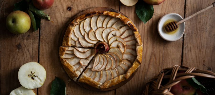 Tarte de maçã vista de cima com maçãs a decorar a mesa de madeira
