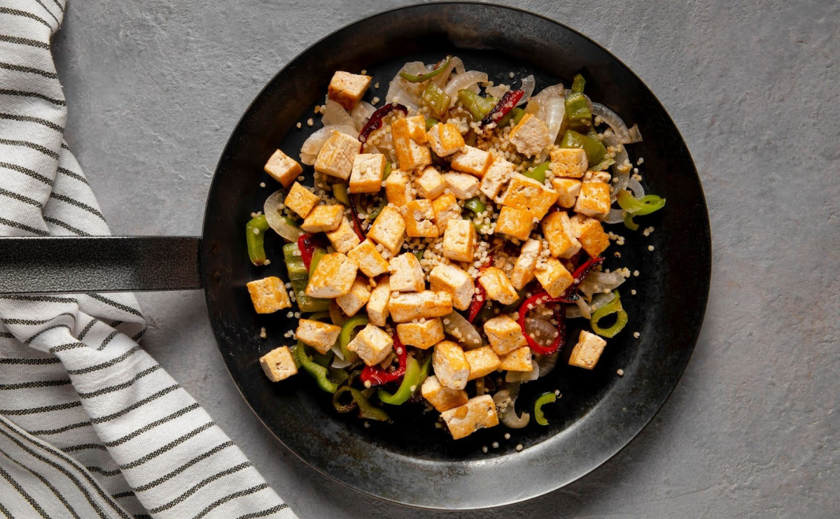 Frigideira com tofu salteado com legumes e quinoa sobre mesa cinzenta