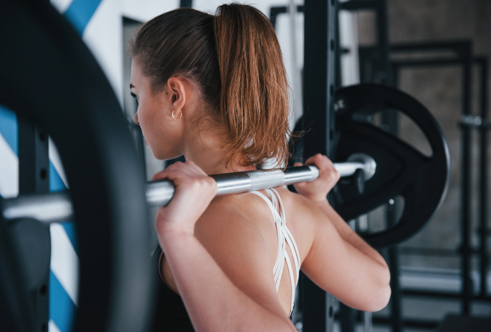 Mulher no ginásio a fazer um exercício de costas com barra