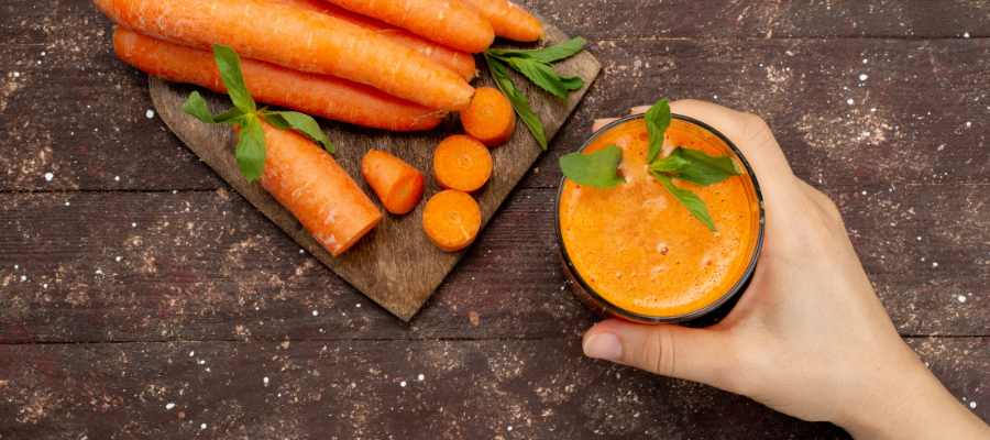 tábua com cenouras e mão a segurar copo com sumo de cenoura