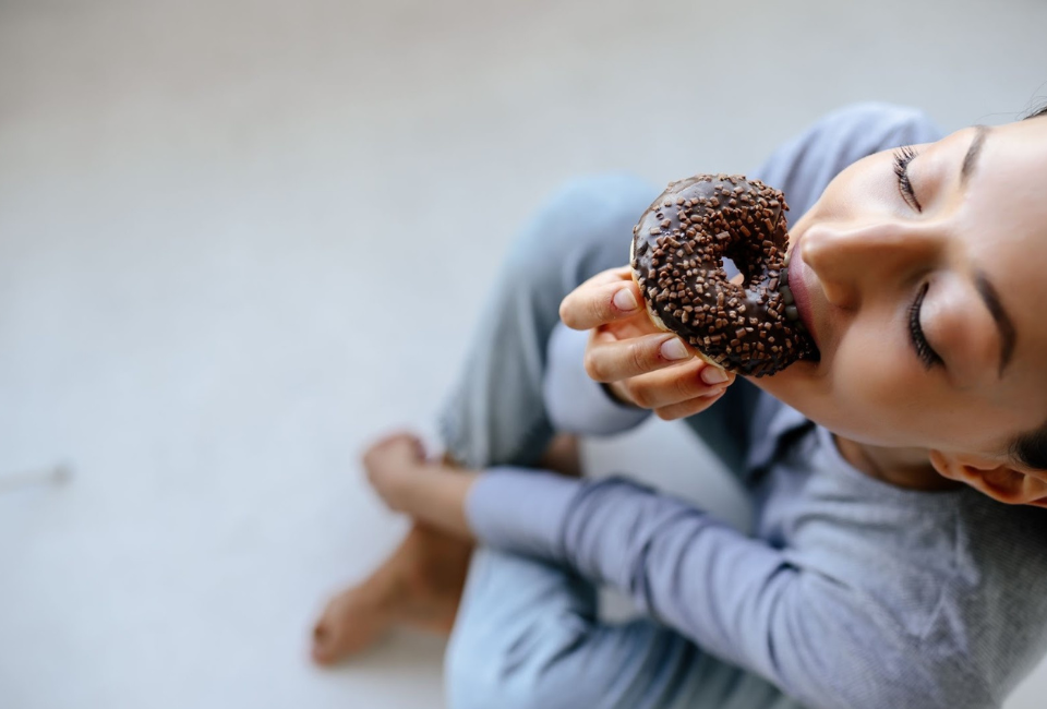 mulher sentada no chão a comer um donut de chocolate