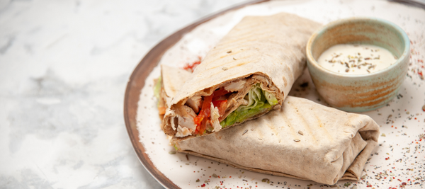 Prato com um wrap de frango e uma tacinha com molho de iogurte